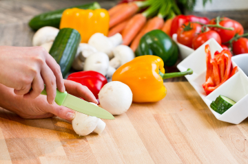 viel frisches Gemüse wie Zwiebeln, Paprika, Gurken, Karotten liegt am Tisch und wird mit einem Küchenmesser geschnitten 